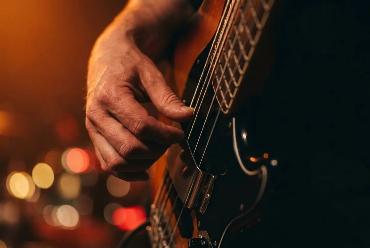 A hand plucking the strings of an electric bass guitar, lit in warm amber light