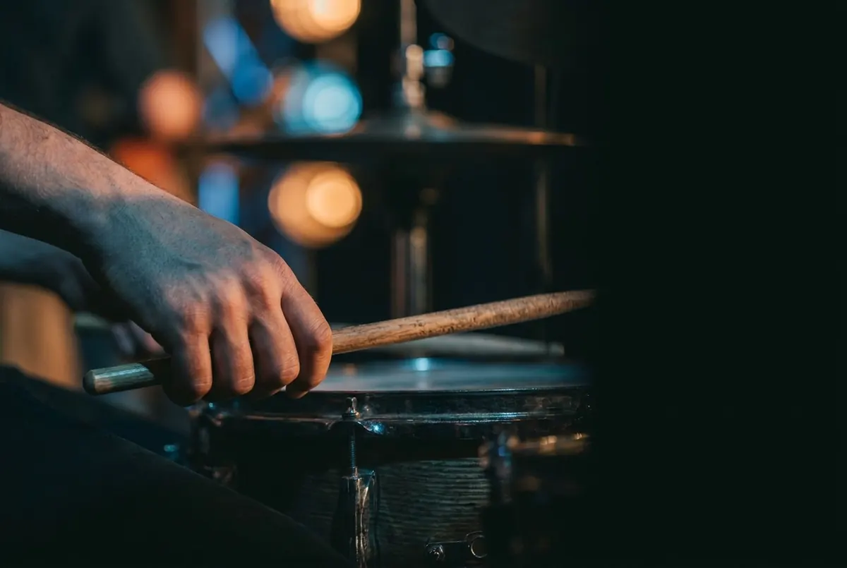 A hand striking a snare drum with a drumstick, lit in cool blue stage light