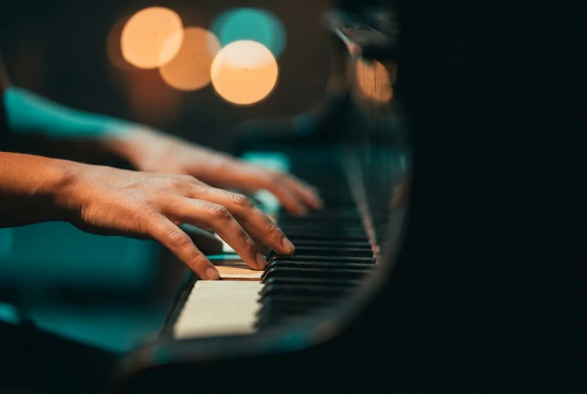 A hand playing across piano keys, lit in teal stage light