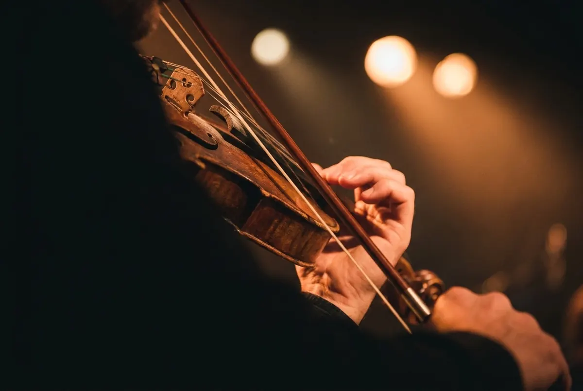 A hand fingering the neck of a violin as the bow is drawn across, lit in warm amber light
